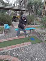 A man in a cap and tracksuit lining up a mini-golf shot