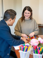 a male and a female sitting at a desk with texta's and paper in front of them doing an activity.