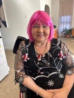 A woman in her 60's with bright pink hair wearing a patterned black dress