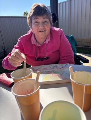 A woman in her 60's wearing a pink jumper, enjoying arts and crafts.