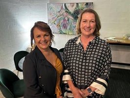 Two women standing together in front of a piece or artwork.