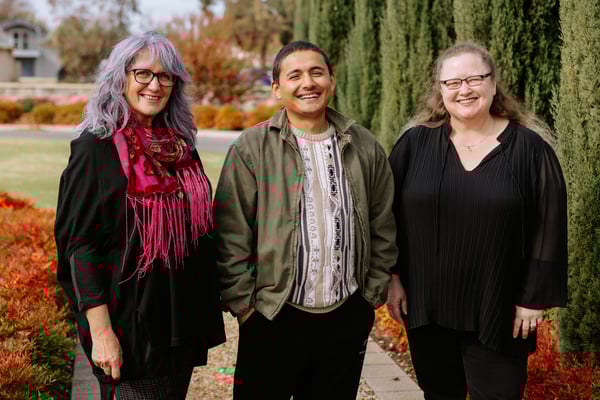 Two women and a man standing together in front of an autumn garden.