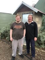A young man standing with his father in front of a shed and green shrubbery.