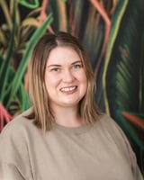 A smiling woman with blonde hair wearing a beige top.