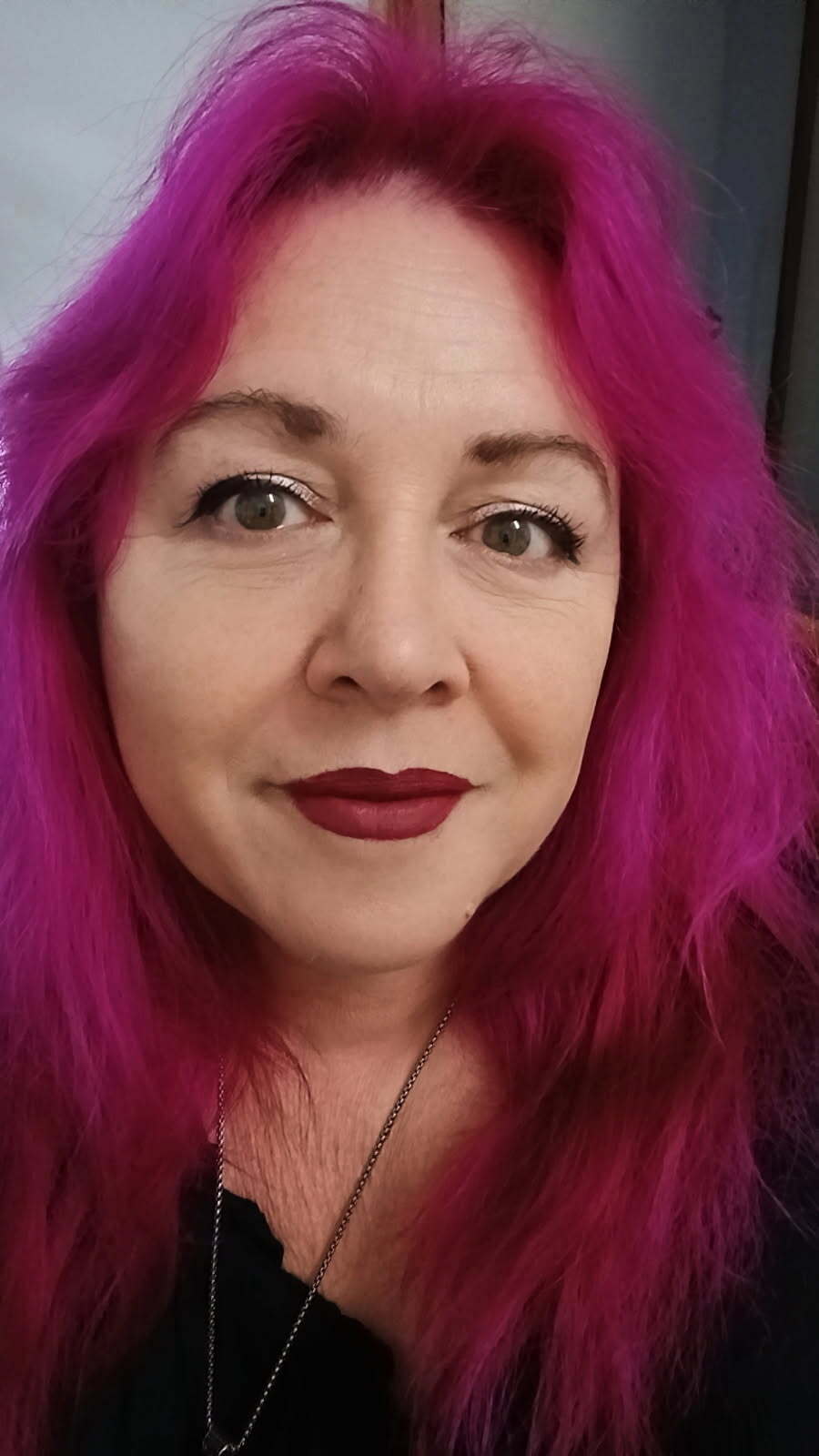 A smiling woman with hot pink, shoulder-length hair.