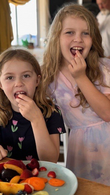 two girls facing the camera eating fruit from a plate