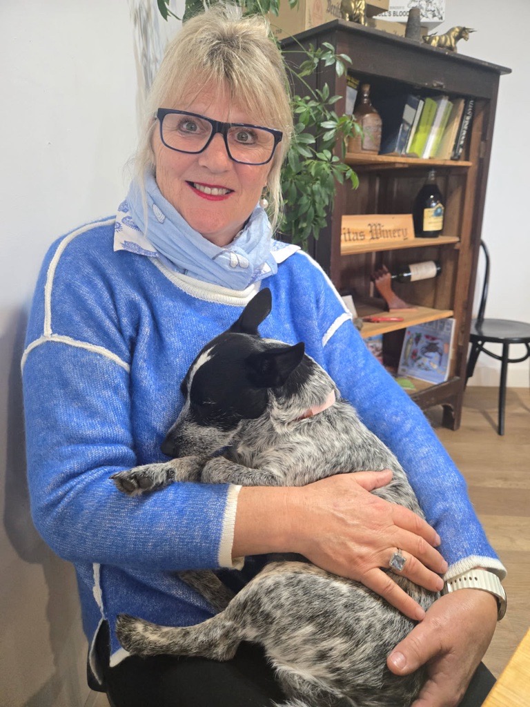 A woman in a blue jumper holding a blue cattle dog puppy.