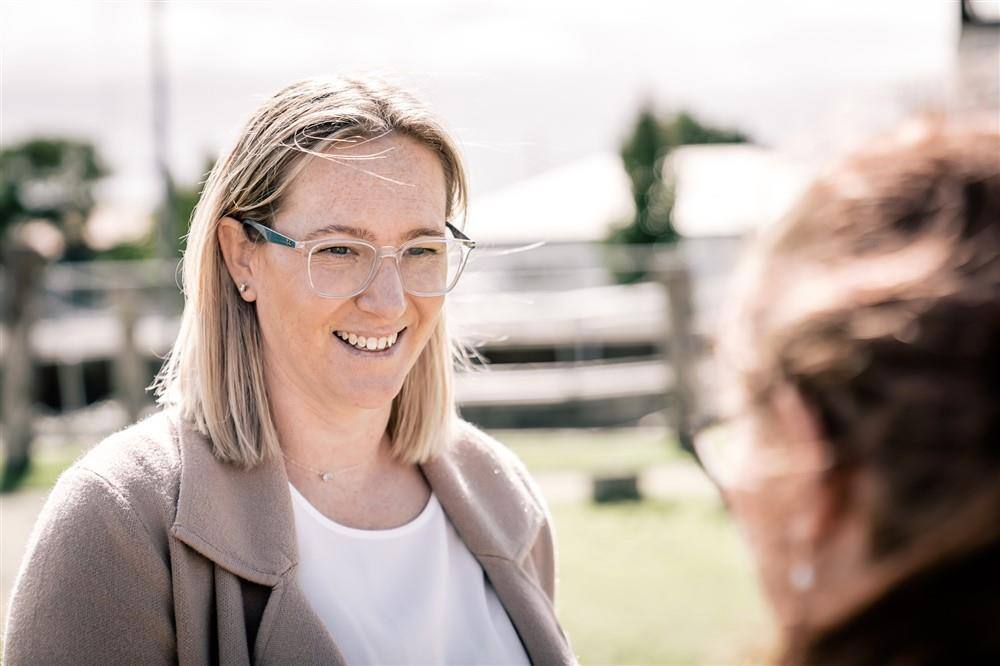 Woman with blonde hair and glasses , smiling at a person standing opposite