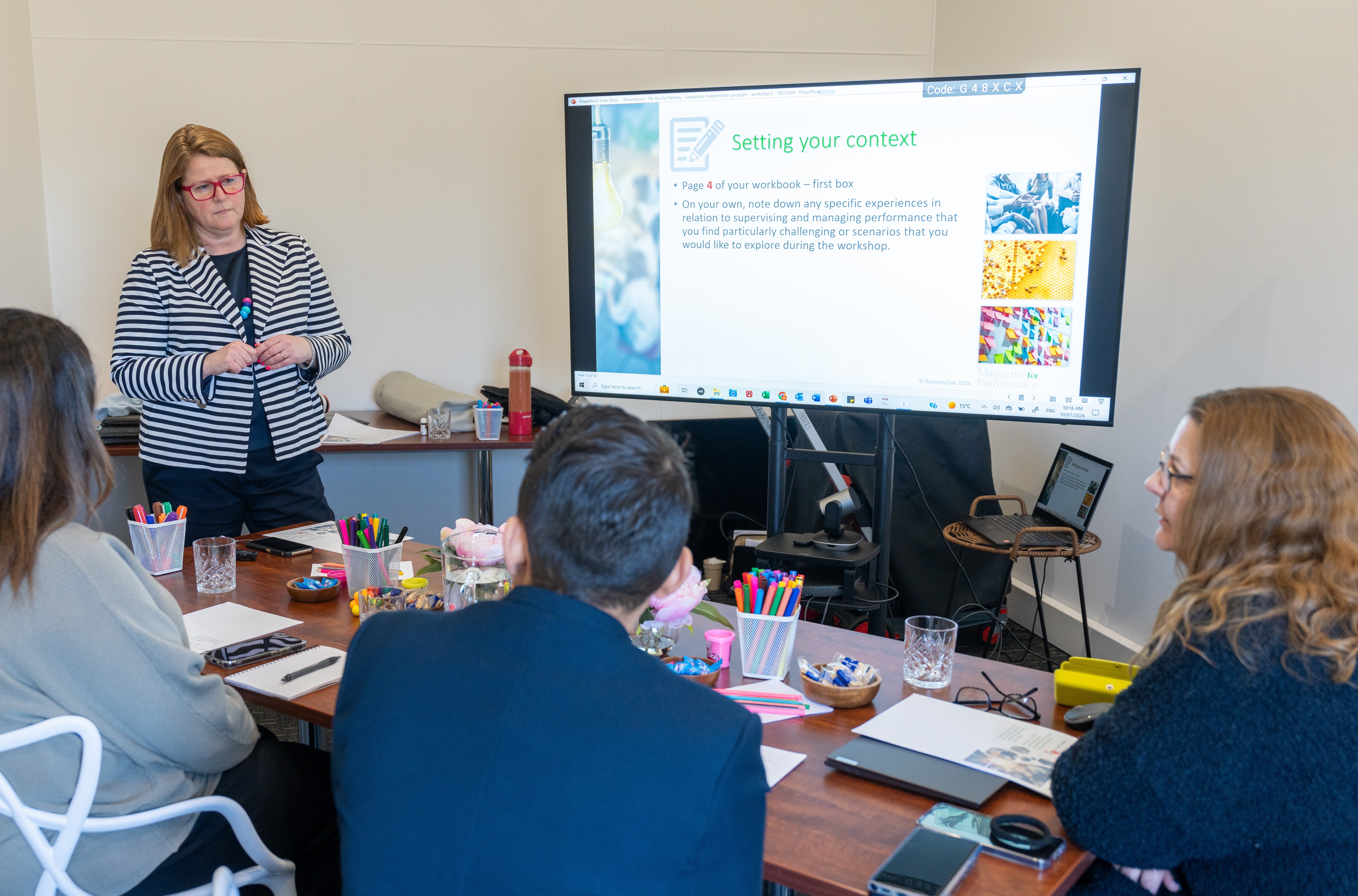 A team of workers sitting around a table while a presenter conducts training with a large screen.