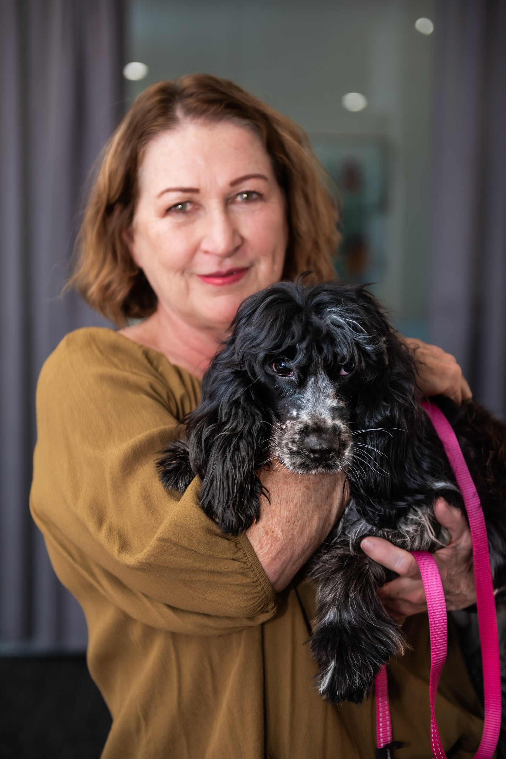 A smiling woman in a yellow top holding a black cocker spaniel dog.