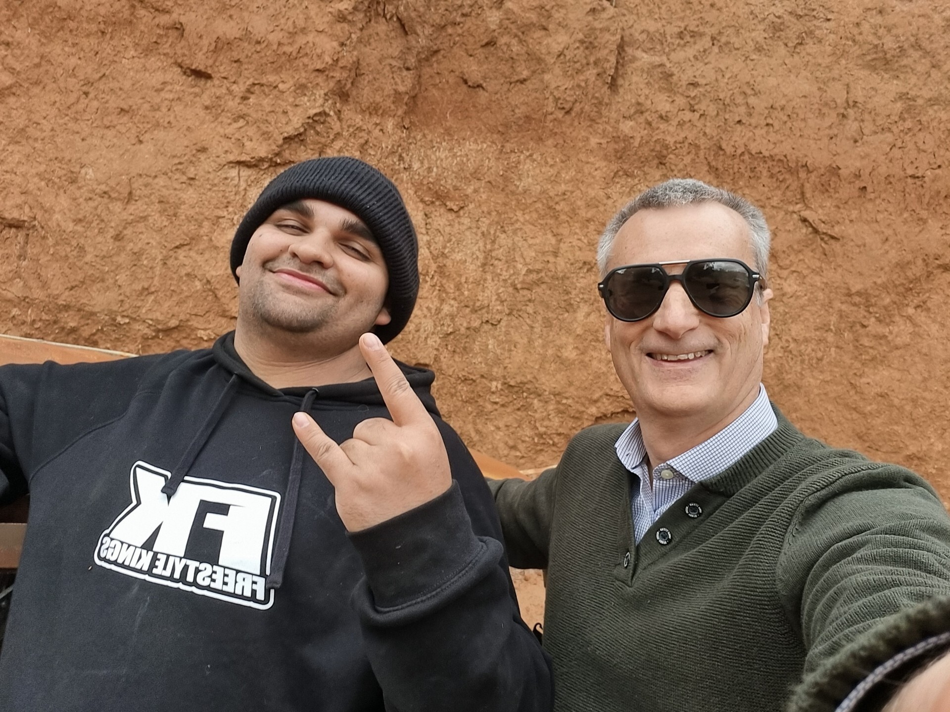 Two smiling men standing in front of a tan cliff face.